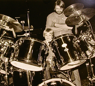 A very young Christopher Swist, under the watchful eye of his father, trying his hand on the stage drum set during a 1979 Chuck Mangione tour.