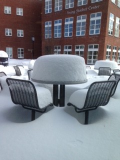 Chairs and tables are covered in snow in front of the student center