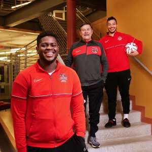 Keene State students and soccer players stand with Coach Rick Scott in the TDS Center