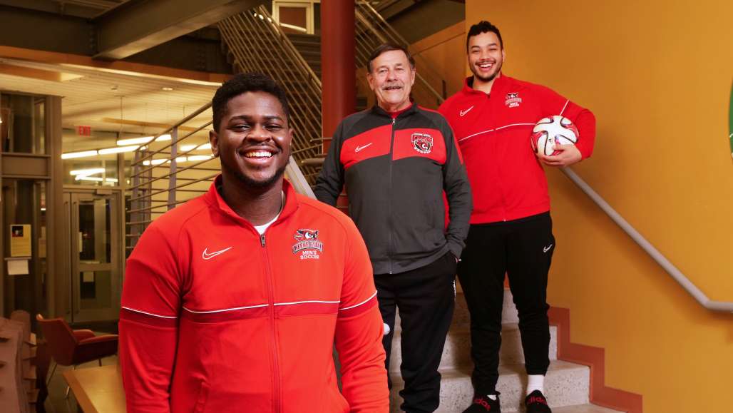 Keene State students and soccer players stand with Coach Rick Scott in the TDS Center