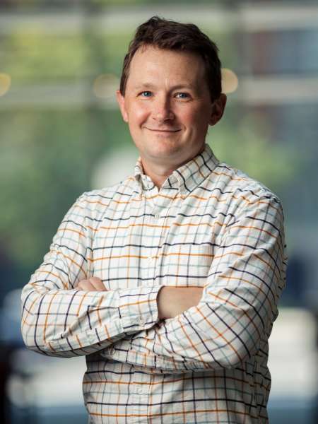 A man stands facing the camera, smiling with his arms crossed over his chest