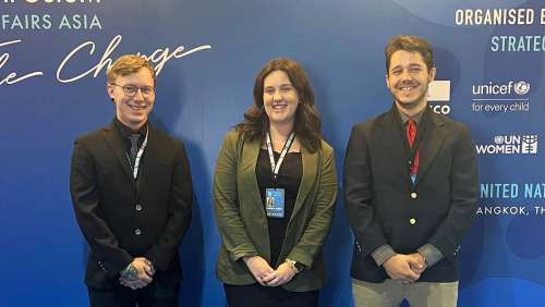 Three students pose in front of a blue background at a symposium