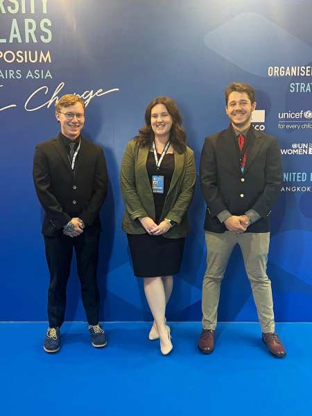Three students pose in front of a blue background at a symposium